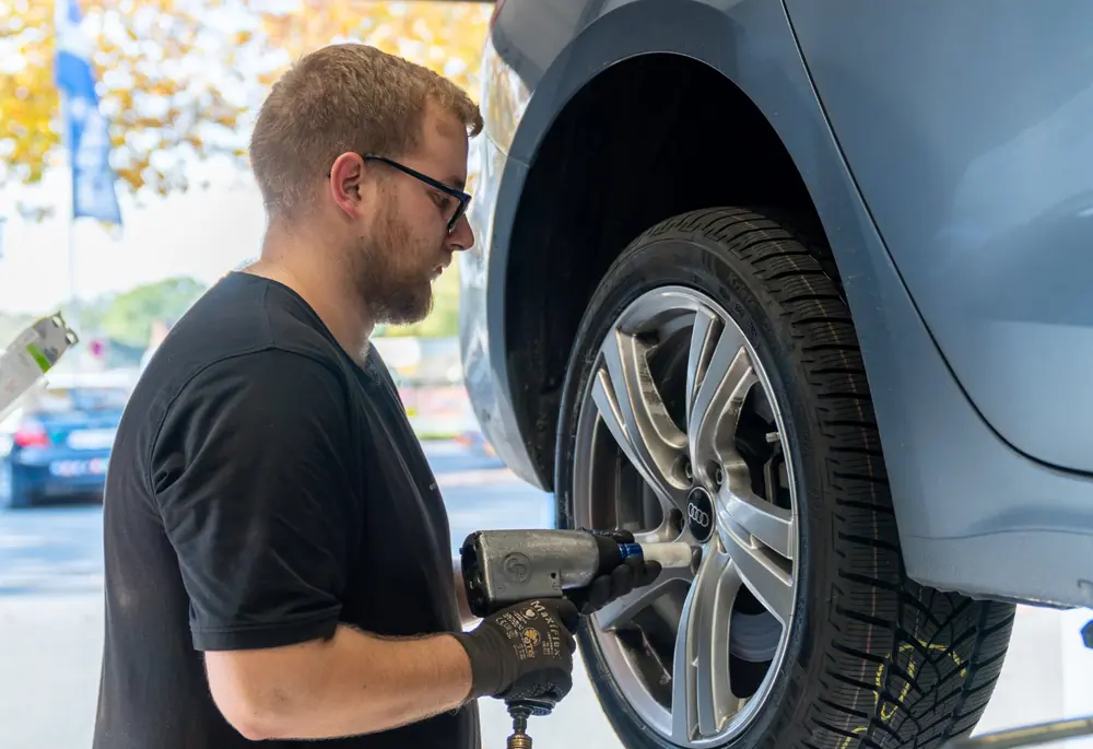 Fahrzeug auf der Hebebühne in der Werkstatt von ProTire, Mechaniker am Rad